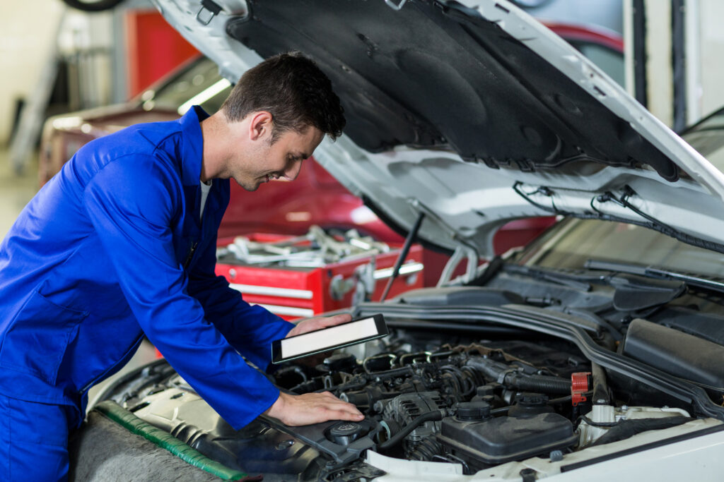 Mechanic using digital tablet while servicing car engine in repair garage